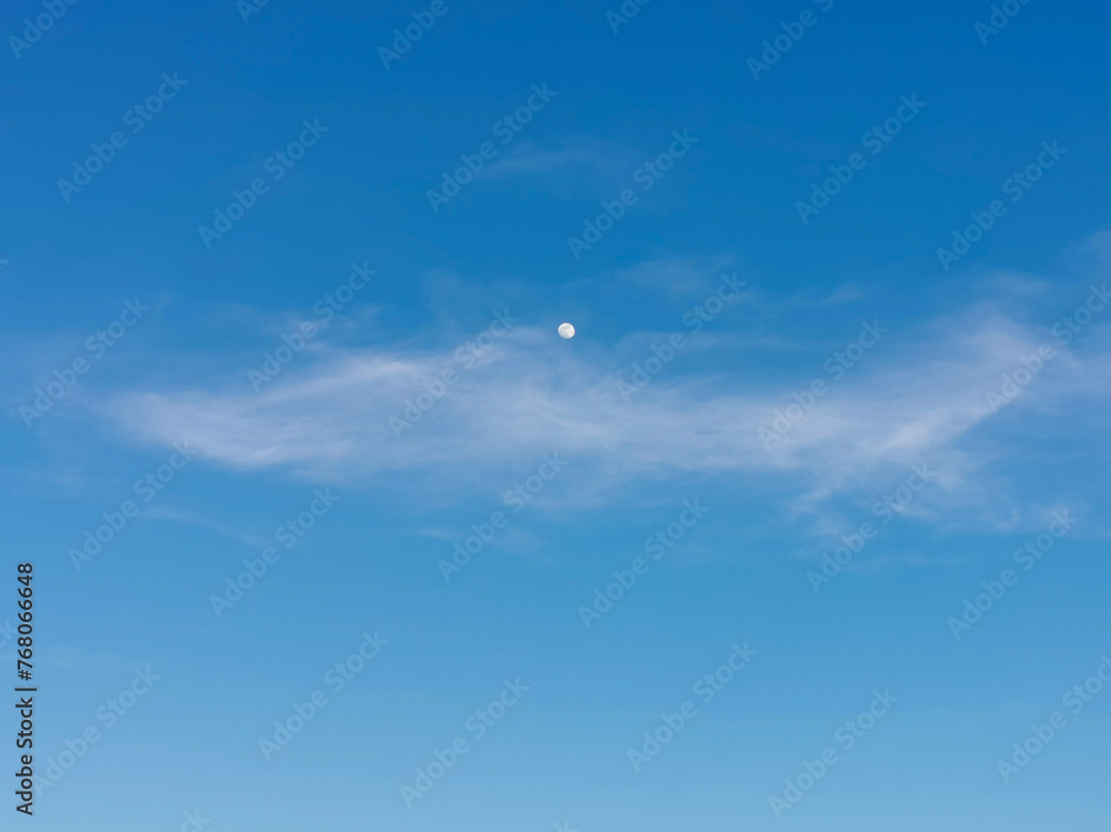 La Luna di giorno nel cielo azzurro dietro al velo di una nuvola