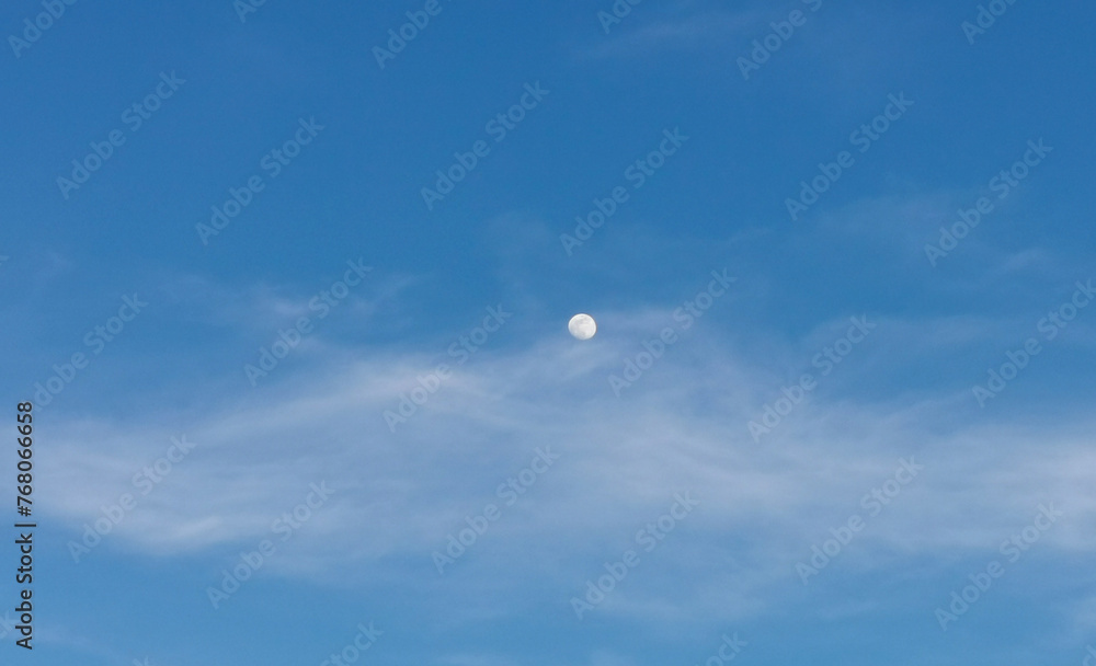 La Luna di giorno nel cielo azzurro dietro al velo di una nuvola La Luna di giorno nel cielo azzurro dietro al velo di una nuvola