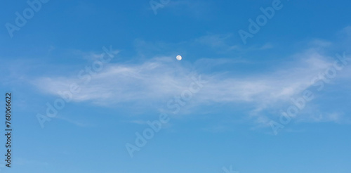 La Luna di giorno nel cielo azzurro dietro al velo di una nuvola photo