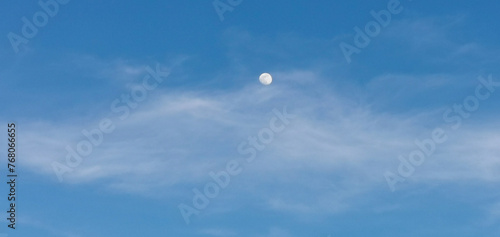 La Luna di giorno nel cielo azzurro dietro al velo di una nuvola photo