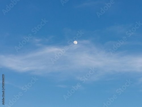 La Luna di giorno nel cielo azzurro dietro al velo di una nuvola