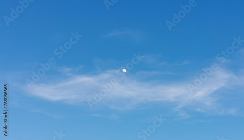 La Luna di giorno nel cielo azzurro dietro al velo di una nuvola 