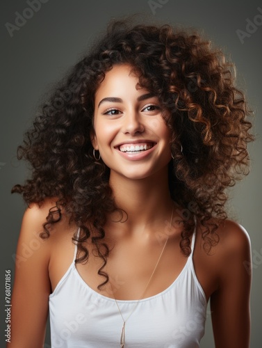 A joyful young woman with voluminous curly hair and a bright smile poses for the camera
