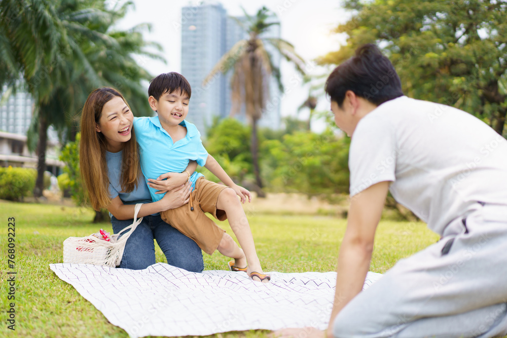 Happy cheerful Asian family with father, mother, and little son enjoy picnic together in a weekend at a park. Happy cheerful Asian family with father, mother, and little son enjoy picnic together in a weekend at a park.