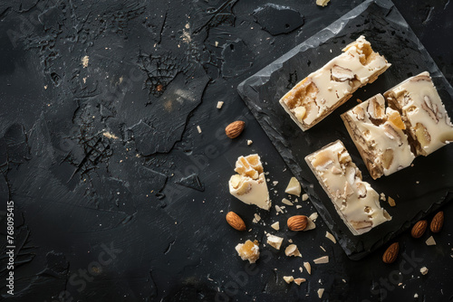 Top view white chocolate nougat with almonds and candied fruit on dark background, free space for text