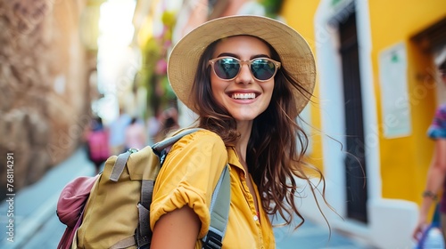 Young attractive woman with long brown hair smiling wearing a yellow shirt, straw hat and sunglasses with a backpack on her shoulder standing in a nar photo