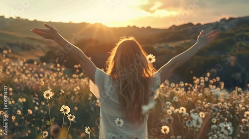 carefree woman standing with arms outstretched in a field of flowers at sunset
