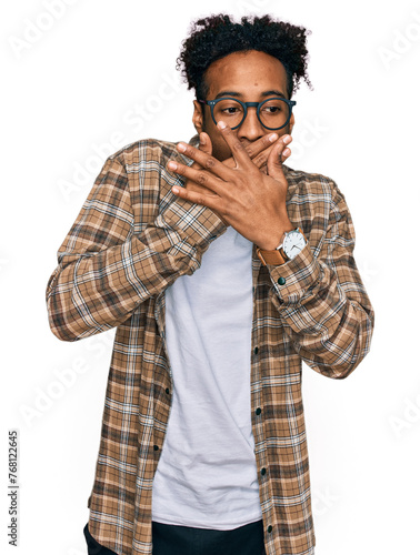 Young african american man with beard wearing casual clothes and glasses shocked covering mouth with hands for mistake. secret concept.