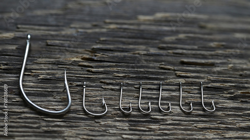Steel fishing hooks of various sizes on a background of rough wood texture.