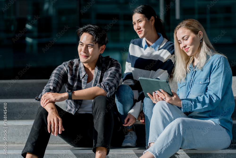 Fototapeta premium Group of happy young diverse colleagues talking and having fun together outdoors on college campus. Happy teenage students talking outside high school building. People in their leisure time.