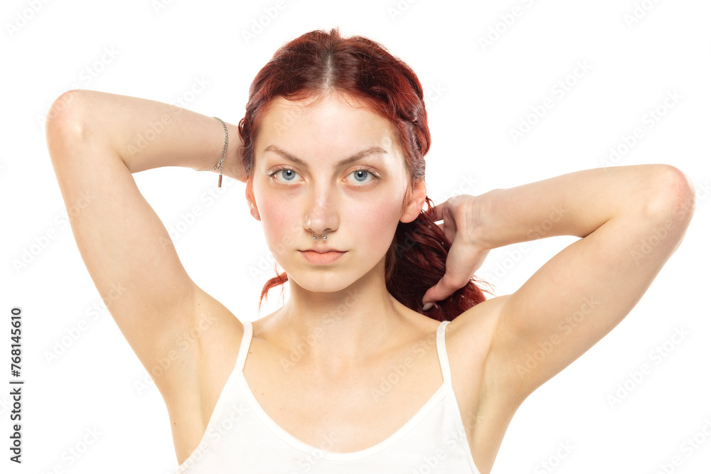 Portrait of a young serious woman without makeup tying her long red wavy hair on a white background