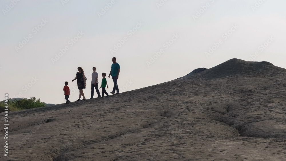 Silhouette of big family with kids going down the hill after visiting the Muddy Volcanoes in Buzau area, Romania