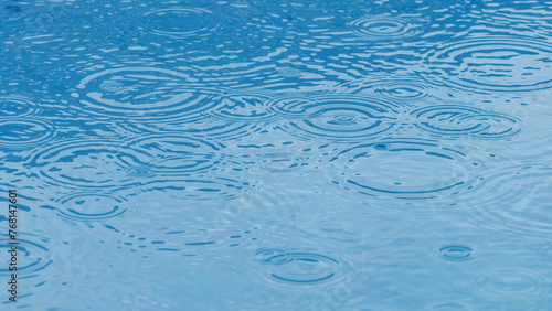 Rain drops falling making circle ripples at the surface of blue water