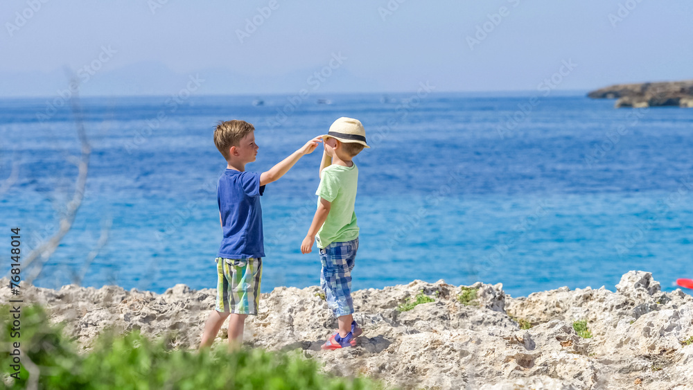 Boy arranging the hat of his younger brother for sun protection on the coast of the seaside Boy arranging the hat of his younger brother for sun protection on the coast of the seaside