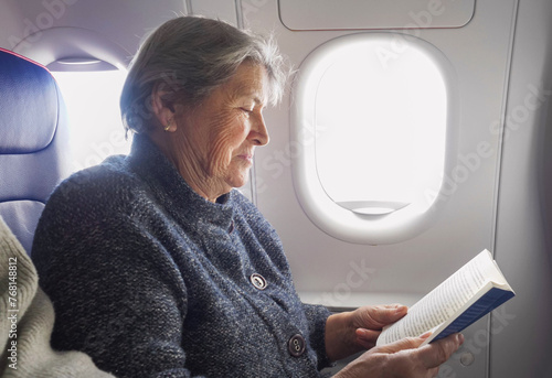 Elderly woman enjoys reading a book in the airplane during the flight