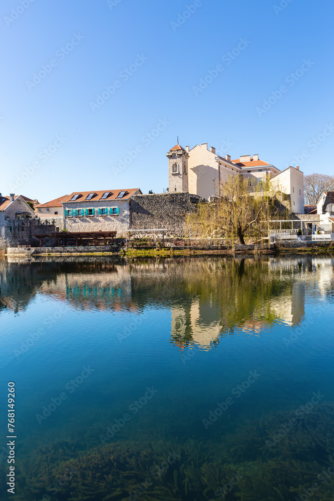 Calm river reflects old Trebinje town with Sahat Kula tower and museum building in clear blue tones, embracing minimalist aesthetic. Trebinje, Bosnia and Herzegovina