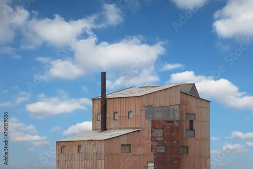 tall building of an old factory with a chimney against a background of blue sky with clouds