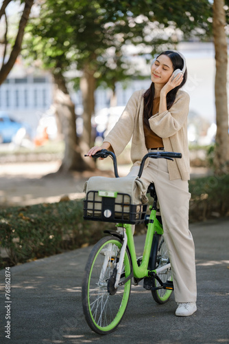 Young asian woman using headphones while riding bicycle in city park