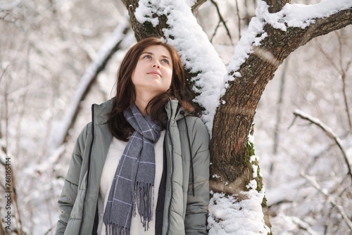 young woman in winter clothes lean on tree covered with snow, girl walking in snowy forest enjoying beautiful nature