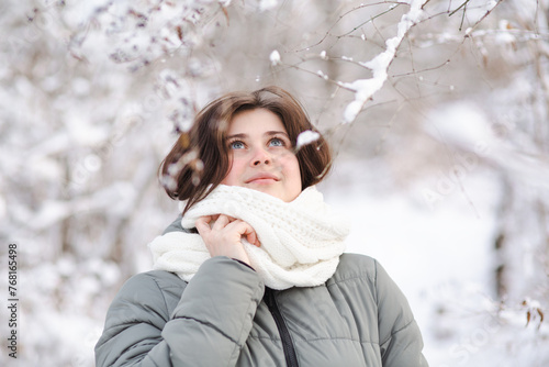 young woman looking up on winter nature, pretty beautiful girl among trees covered with snow walking in white forest and enjoying