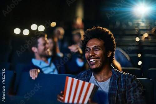 Smiling young man watching a movie in theater with popcorn photo