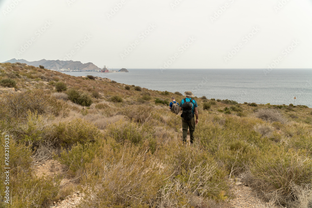 Back view, two hikers walking near the sea. Back view, two hikers walking near the sea.