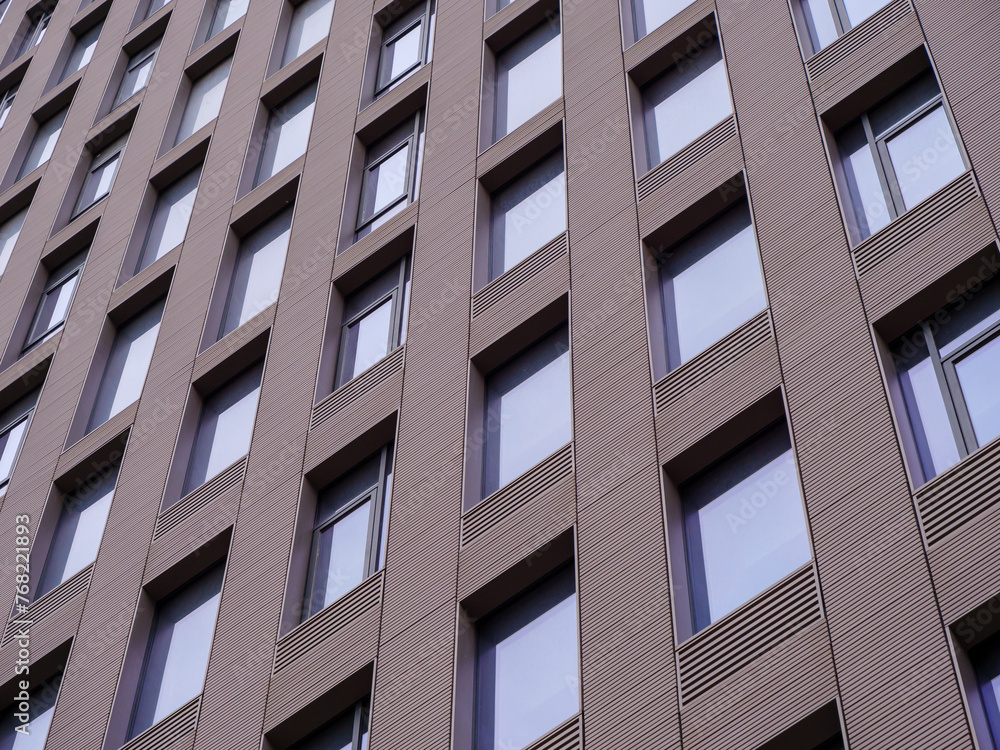 Angular view of a contemporary building showcasing repetitive pattern of windows and textured cladding. Angular view of a contemporary building showcasing repetitive pattern of windows and textured cladding.
