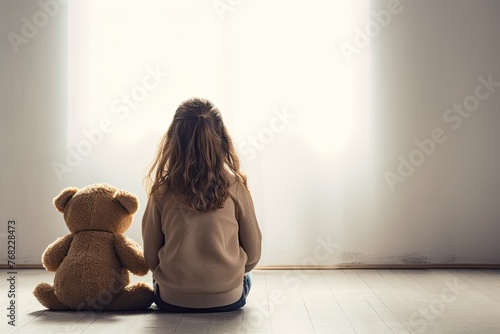 Little autistic girl with teddy bear sitting on floor at empty room. Autism concept