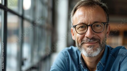 Confident businessman in glasses smiling for close-up portrait in modern office setting.
