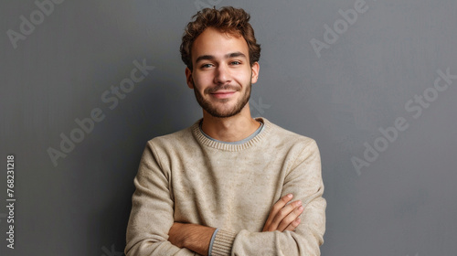 Happy young man with folded arms posing against gray background. © Noreen