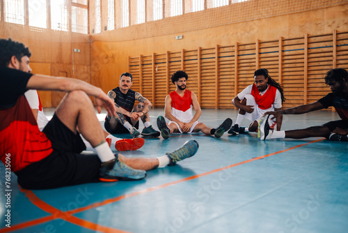 An interracial basketball team is sitting on court and having training. © Zamrznuti tonovi