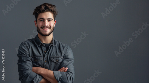 Smiling casual young man posing with folded arms against gray background.