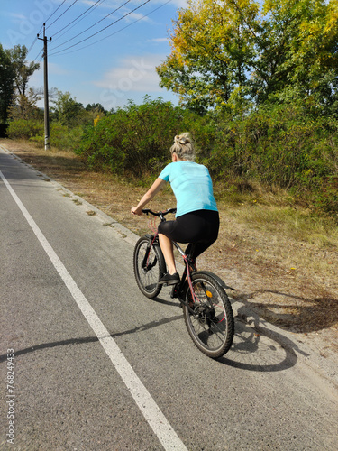 A young woman rides a bicycle along the asphalt road in the park. Active recreation in nature