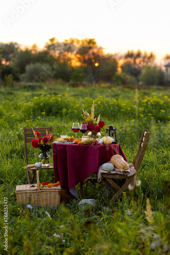 Beautiful elegant outdoor romantic dinner table decor countryside style: pumpkins, candles, flowers, red wine, gourmet cheese board. Cozy garden interior, open air party event. Sunset golden hour
