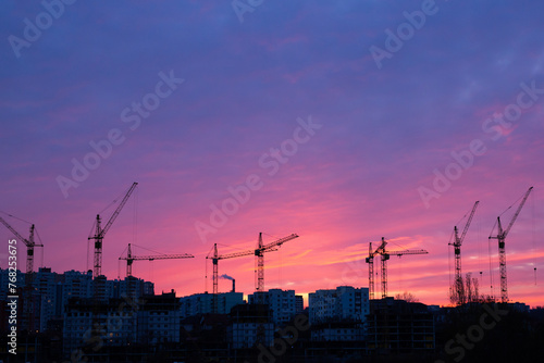 Progress and growth. Tower cranes on building of  many-storeyed house stock photo. Six tall construction cranes stand out as dark silhouettes against the colorful sky. Urbanization concept.