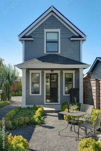 Nestled in the picturesque landscape, this serene gray home exudes tranquility. Surrounded by lush shrubs, the inviting patio area welcomes visitors with its cozy seating arrangement.