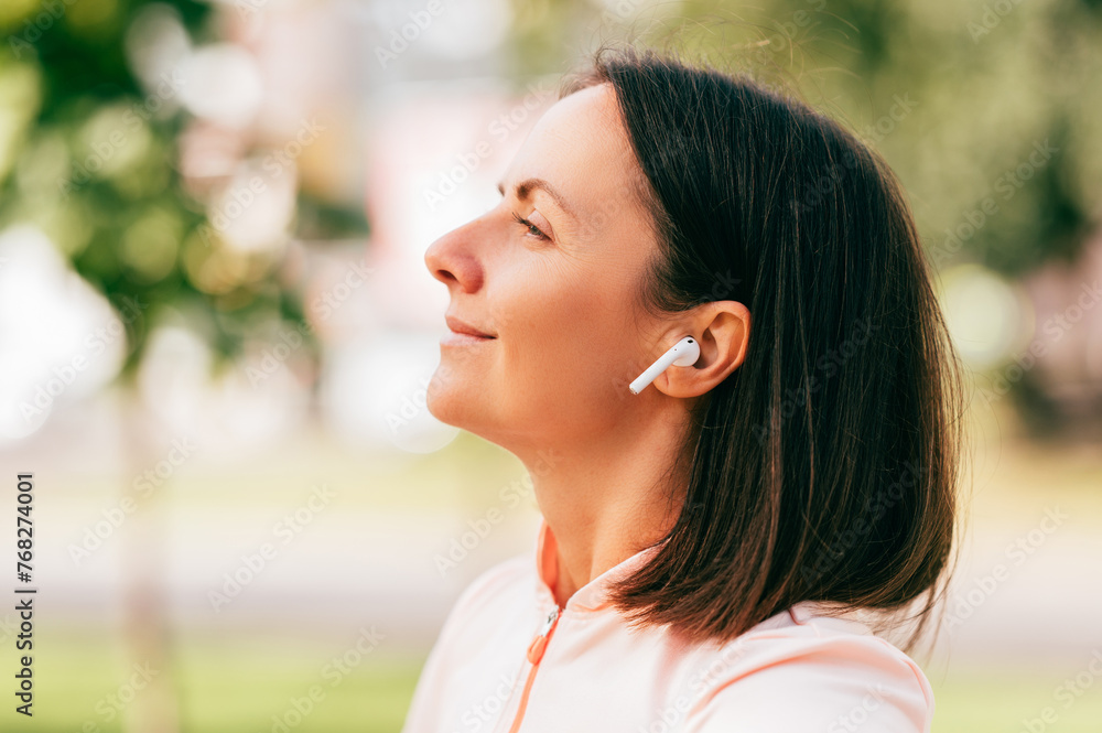Close up outdoors portrait of a smiling middle age woman enjoying a good day while using ear buds. Close up outdoors portrait of a smiling middle age woman enjoying a good day while using ear buds.