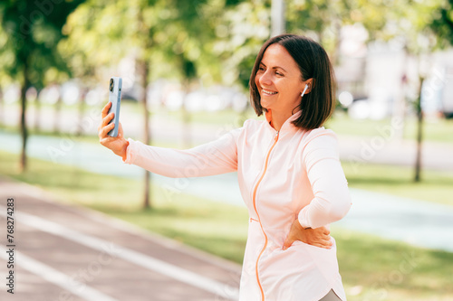 Outdoors portrait of a smiling middle age sporty woman taking a picture with her smart phone.