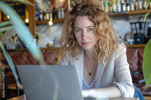 Portrait of young woman using laptop in coffee shop. Female freelancer working on laptop at cafe.
