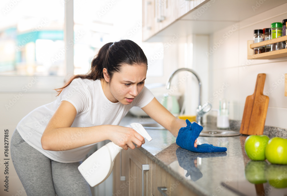 Friendly young woman with rag cleaning kitchen at home