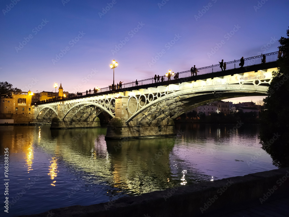 Beautiful bridge in night illumination over the Guadalquivir river at sunset in Seville, Andalusia, Spain