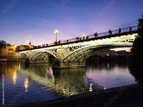 Beautiful bridge in night illumination over the Guadalquivir river at sunset in Seville, Andalusia, Spain