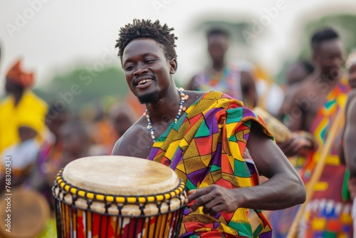 Concentrated African drummer playing a djembe at a cultural event with others in the background