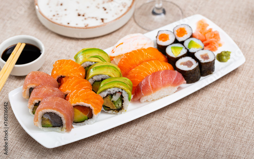 Sushi set con maki with uramaki rolls and salmon nigiri is served in white narrow rectangular plate. Traditional Japanese Asian cuisine, gastronomy tourism
