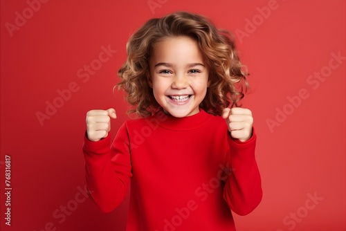 Cheerful little girl with curly hair in a red sweater on a red background.