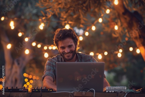 Smiling man uses laptop to DJ at a festive outdoor setting with lights
