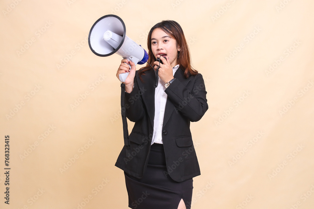 Beautiful formal Asian office woman in suit standing talking candid with mic using megaphone for promo broadcast announcement on yellow background for commercial, advertising and business Beautiful formal Asian office woman in suit standing talking candid with mic using megaphone for promo broadcast announcement on yellow background for commercial, advertising and business