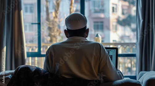 A Muslim man is captured from the rear view  using a laptop while seated on a sofa