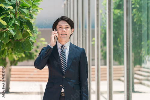 外回り中にスマホで通話するスーツ姿の若いアジア人男性ビジネスマン
