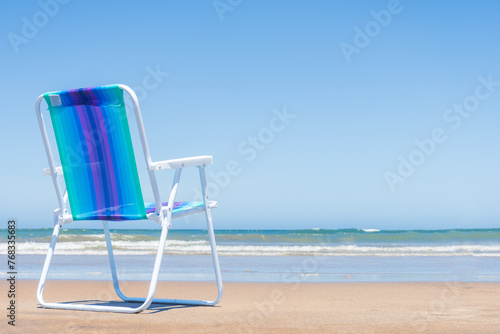 Colorful deckchair with thermos and matte on the sand overlooking the sky and the sea.